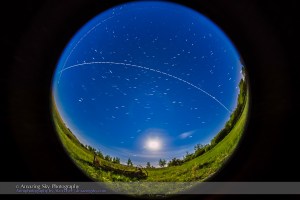 An overhead pass of the International Space Station in a bright moonlit sky on the night of May 31/ June 1, 2015, with the gibbous Moon in to the south, below. The view is looking south, with the ISS travelling from right (west) to left (east) over several minutes. This was the second pass of a 4-pass night, May 31/June 1, starting at 12:44 am MDT this morning.  This is a composite stack of 91 exposures, each 4 seconds at f/3.5 with the 8mm fish-eye lens and ISO 6400 with the Canon 6D. The gaps are from the 1-second interval between exposures. The length of the trails and gaps reflects the changing apparent speed of the ISS as it approaches, passes closest, then flies away. The stars are trailing around Polaris at top. An aircraft supplies the other dashed trail across the top and intersecting with the ISS trail. I stacked the exposures with the Advanced Stacker Actions from StarCIrcleAcademy.com, using the Lighten mode. The ground comes from a Mean blend of just 8 of the exposures to prevent shadows from blurring but to smooth noise.